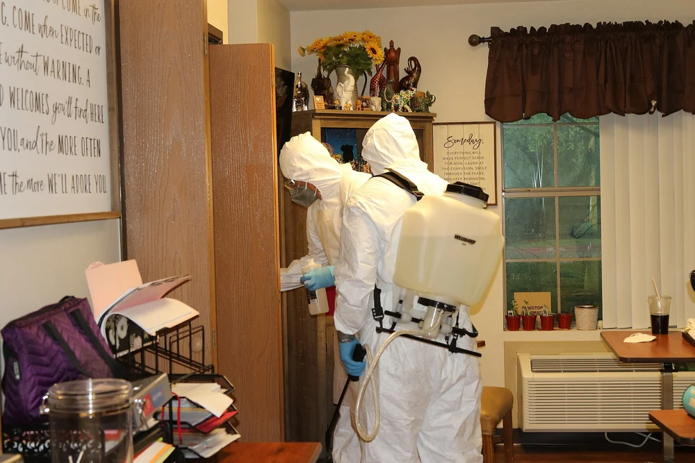 Workers in white protective suits disinfecting a furnished room