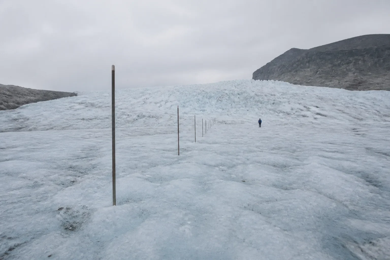 Ablation stakes lead toward a glacier with one distant field worker for scale.